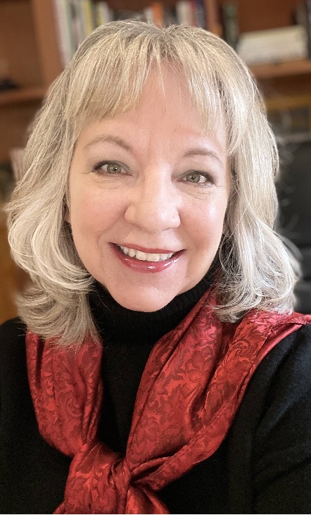 Melanie Davis smiling into the camera, wearing a black sweater and red scarf