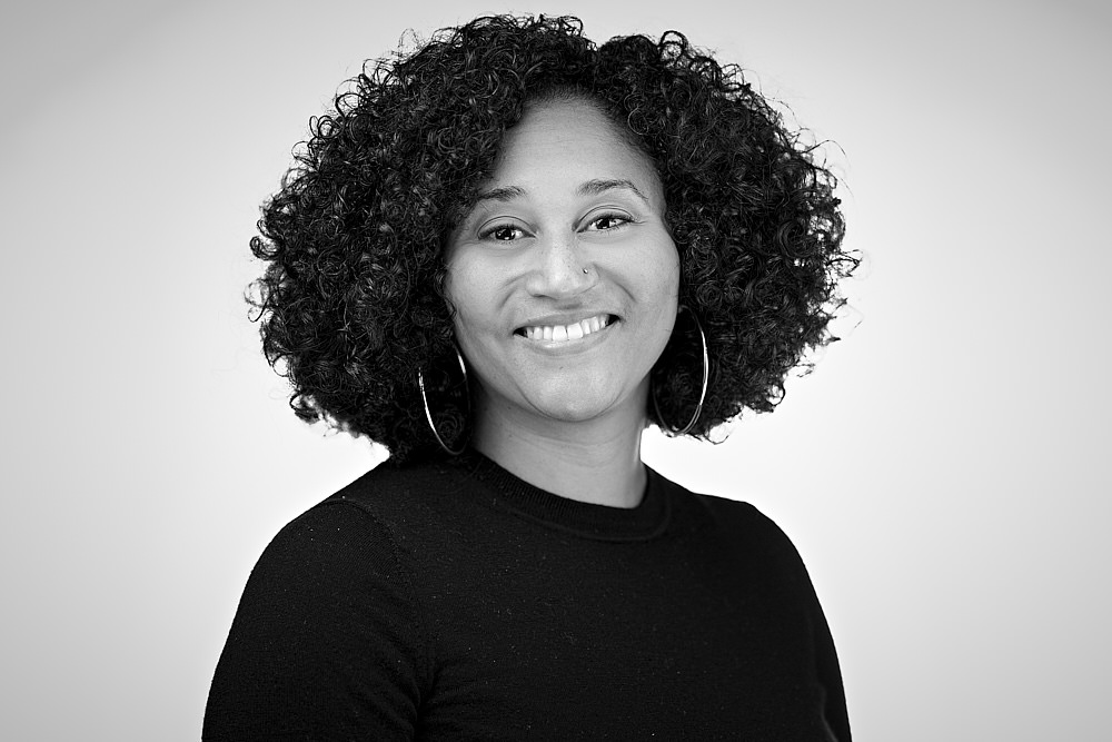 Head shot of Scotney Young, a Black woman with medium length curly black hair, big hoop earrings and a wide smile.